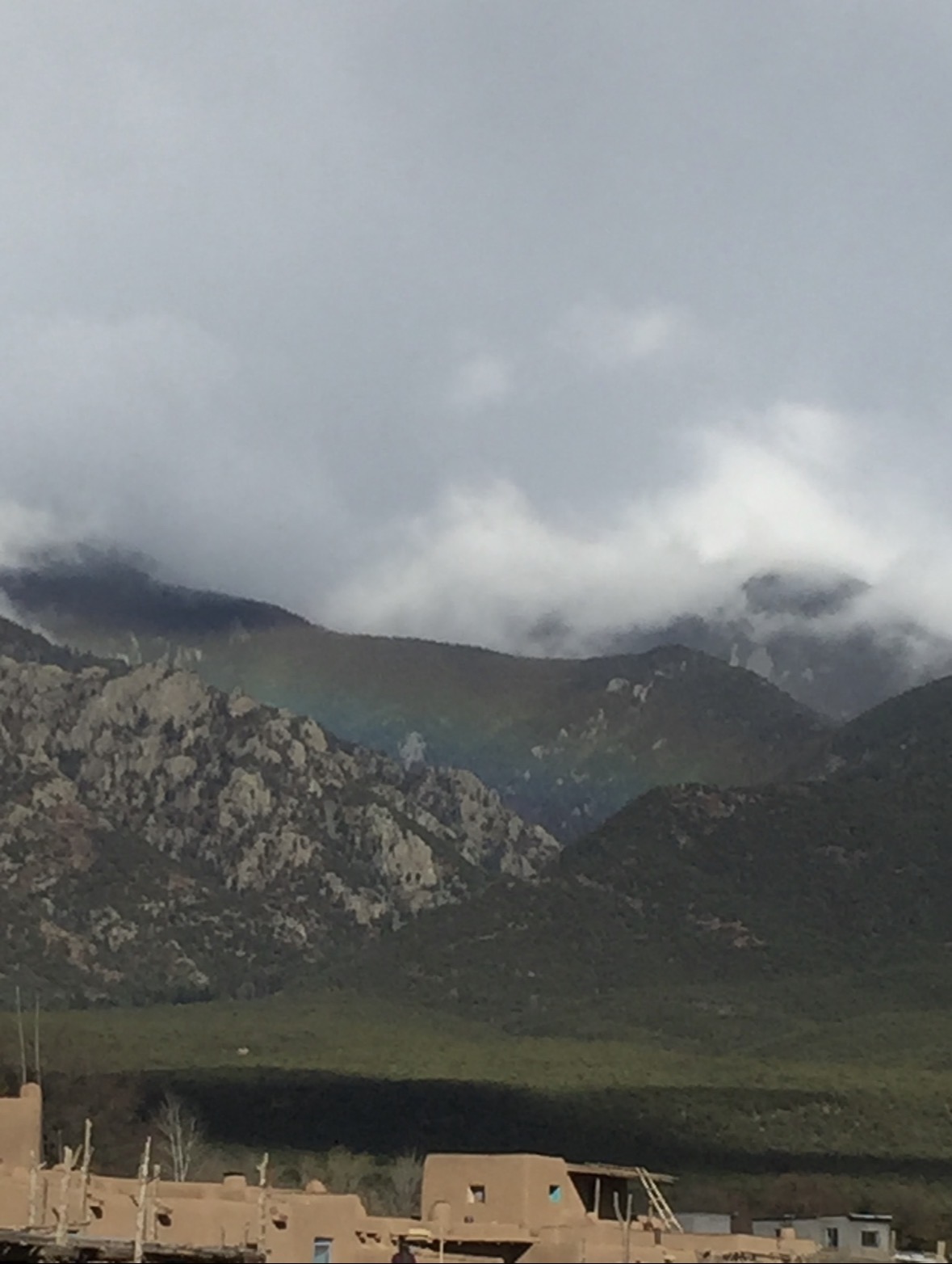 Adobe homes of Taos Pueblo beneath mountains and low cloud